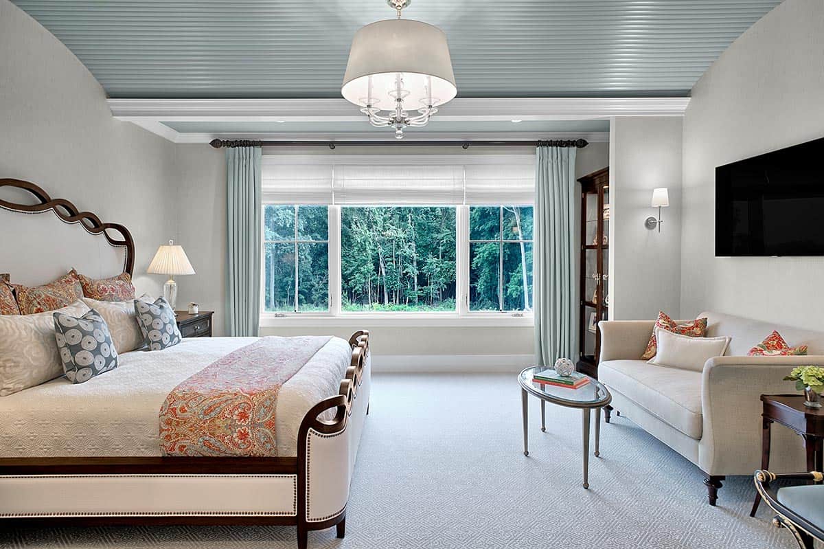 Bedroom with an upholstered bed, blue paneled ceiling, and wooded views