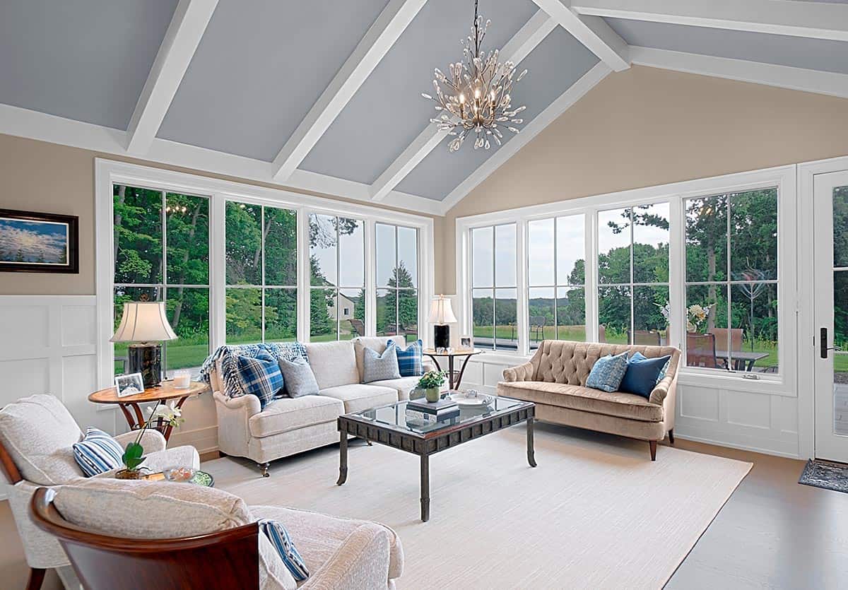 Sunroom with a crystal chandelier, tufted sofas, and wraparound views of the property