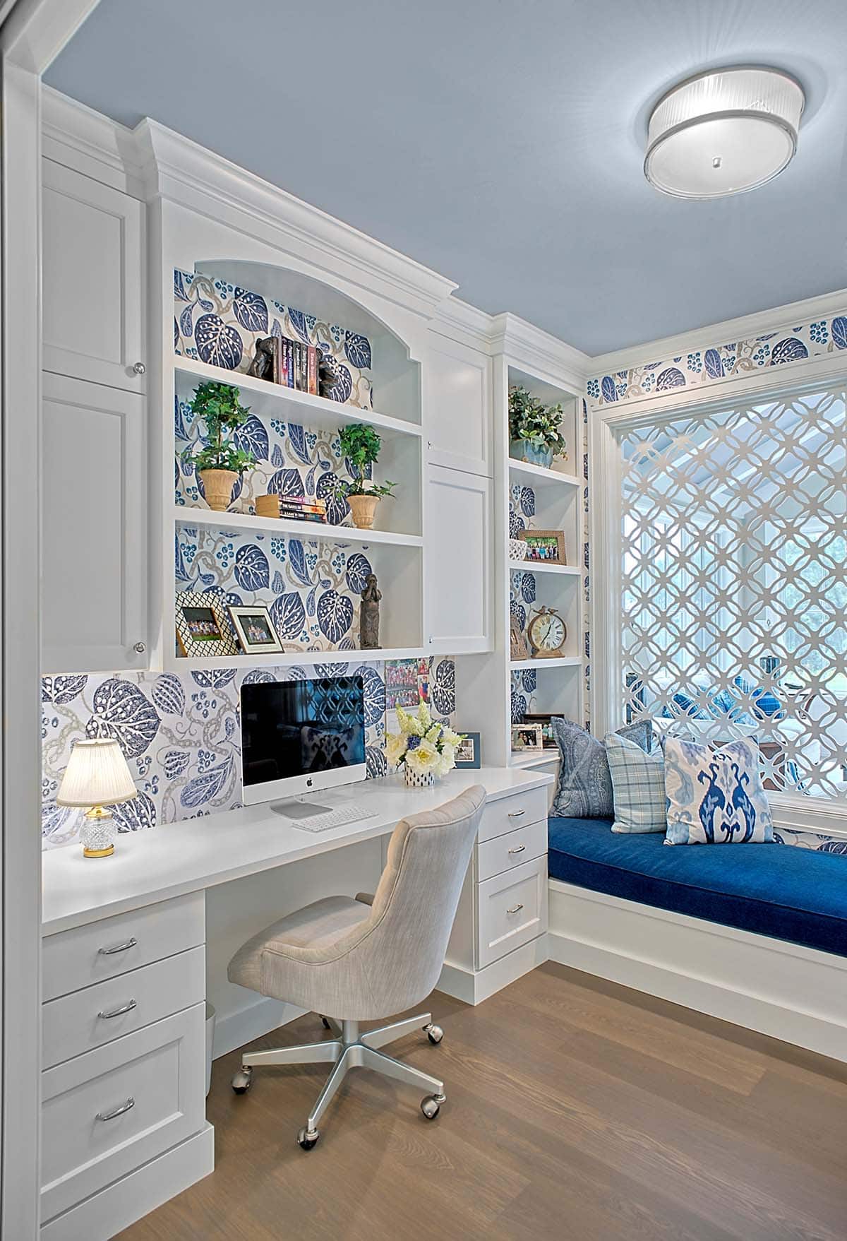 Home office desk area with floral wallpaper and a blue upholstered window seat