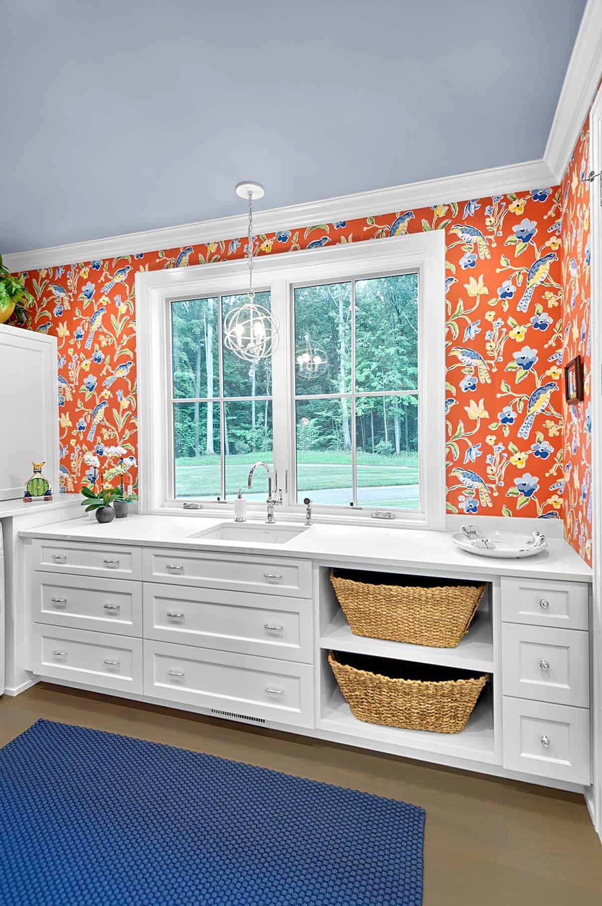 Laundry room sink area with bold orange bird-and-floral wallpaper