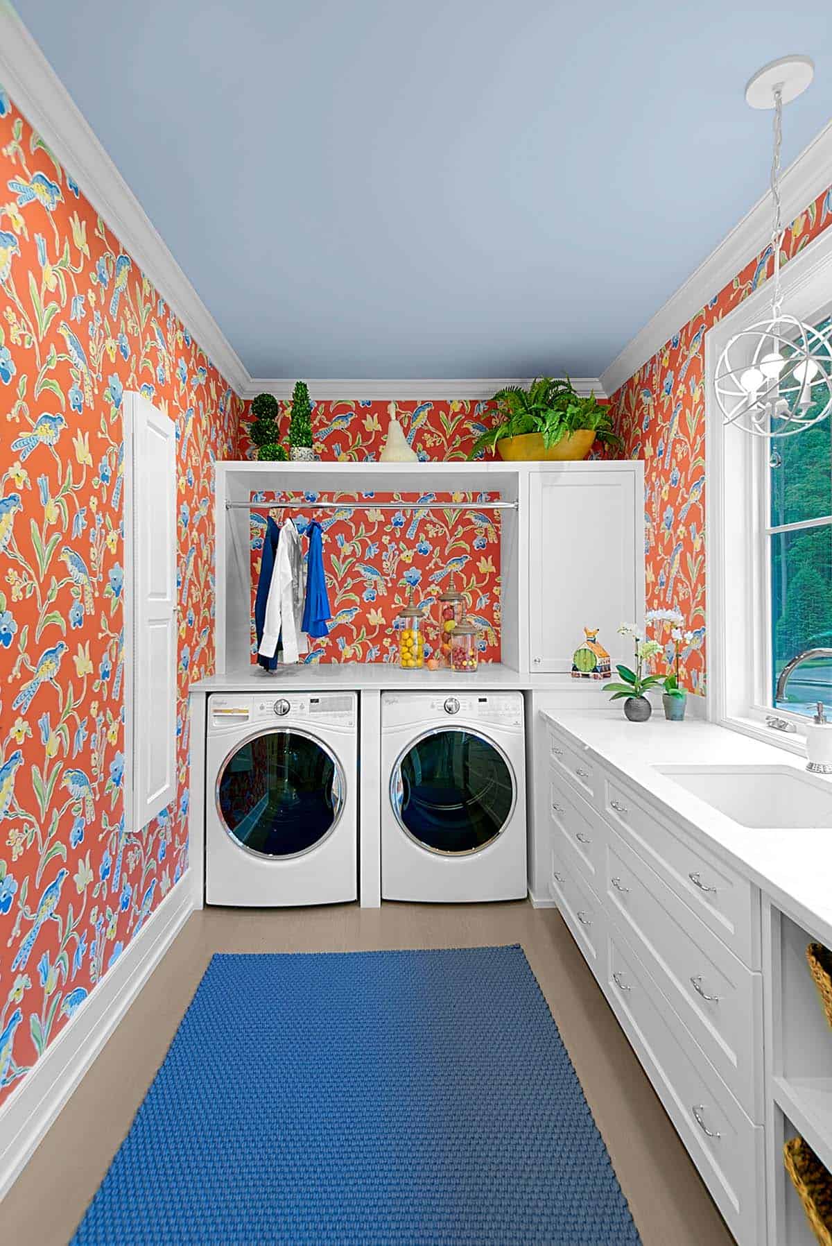Laundry room with front-load washer and dryer beneath vibrant orange wallpaper