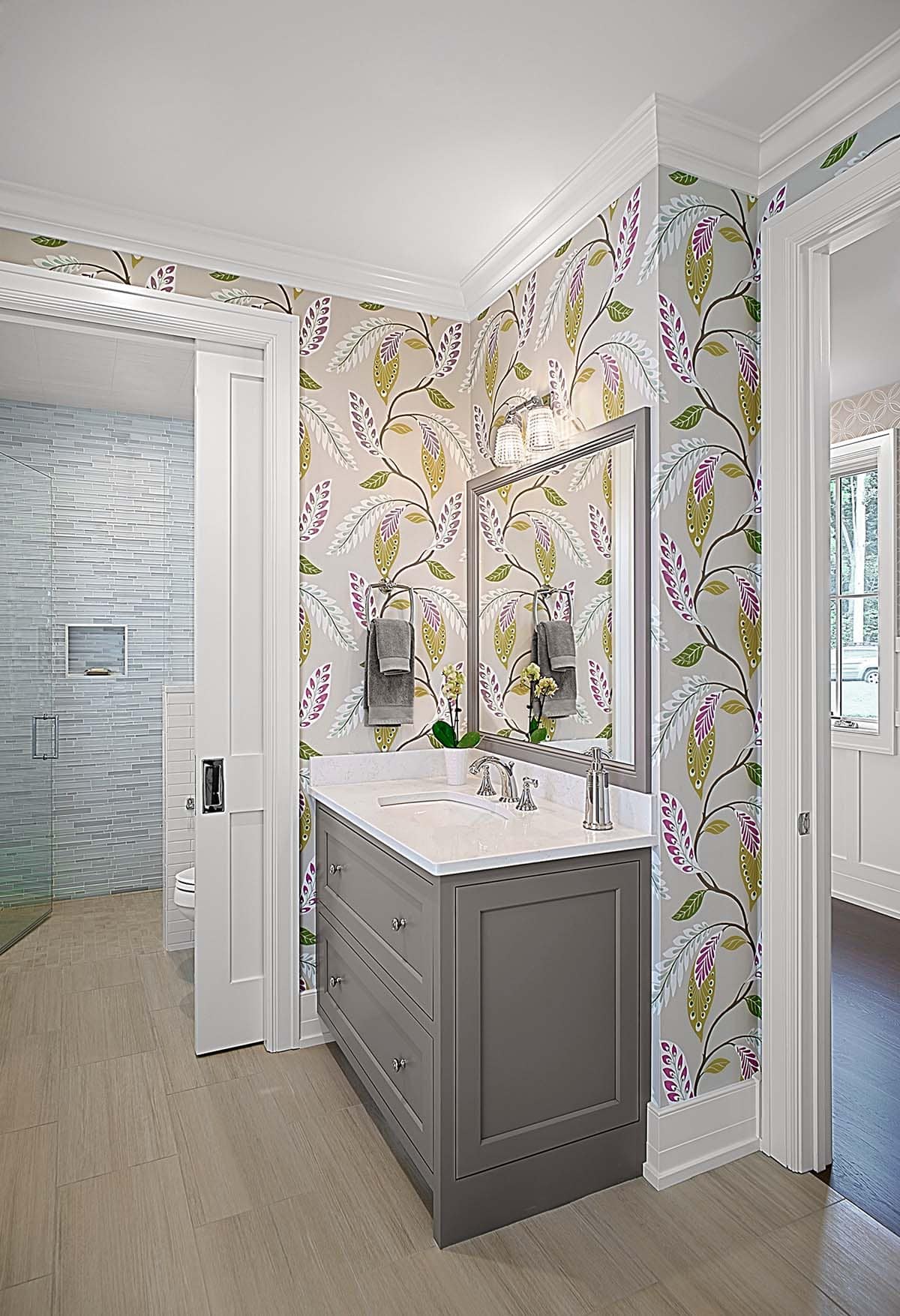 En-suite bathroom vanity with botanical wallpaper and a glass-tiled shower