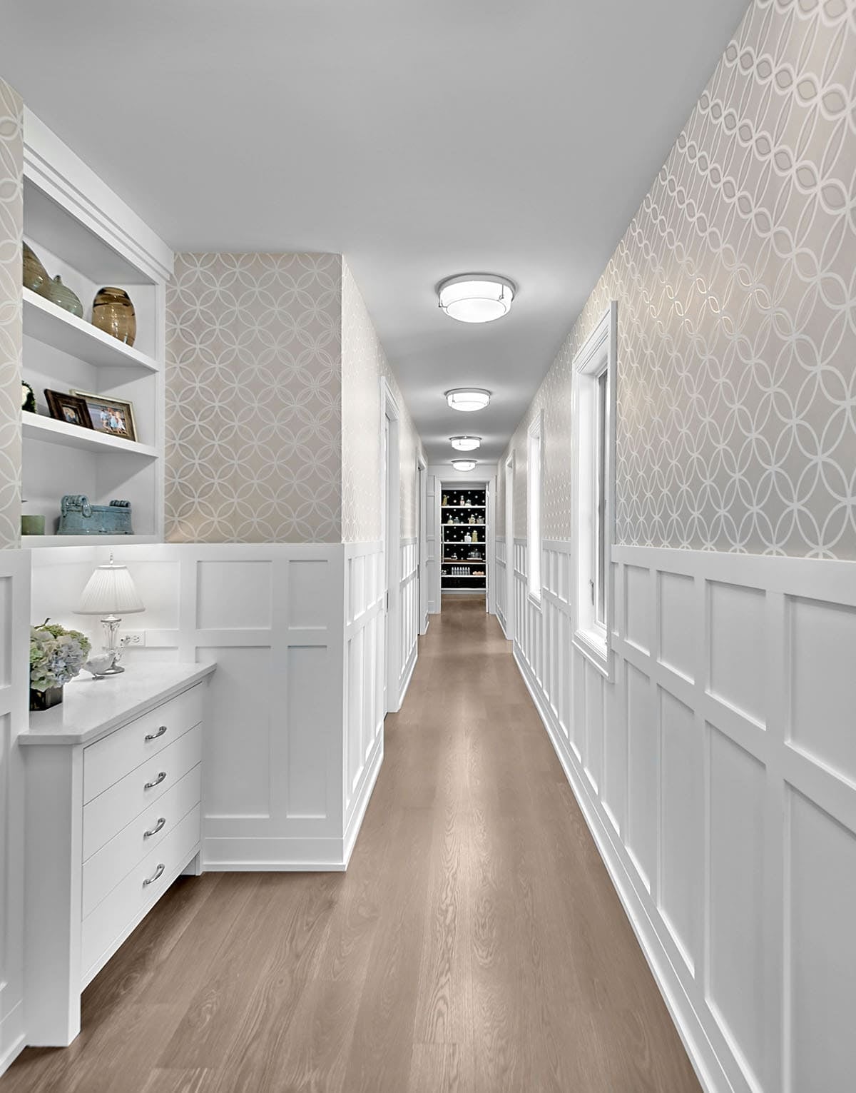 Long hallway with patterned wallpaper, wainscoting, and built-in dresser
