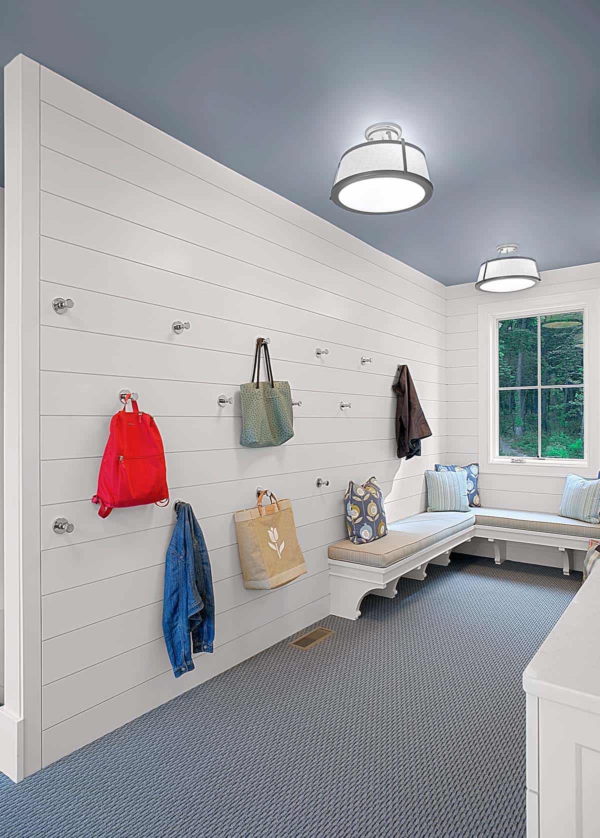 Mudroom wall with wall hooks holding bags and jackets above a bench