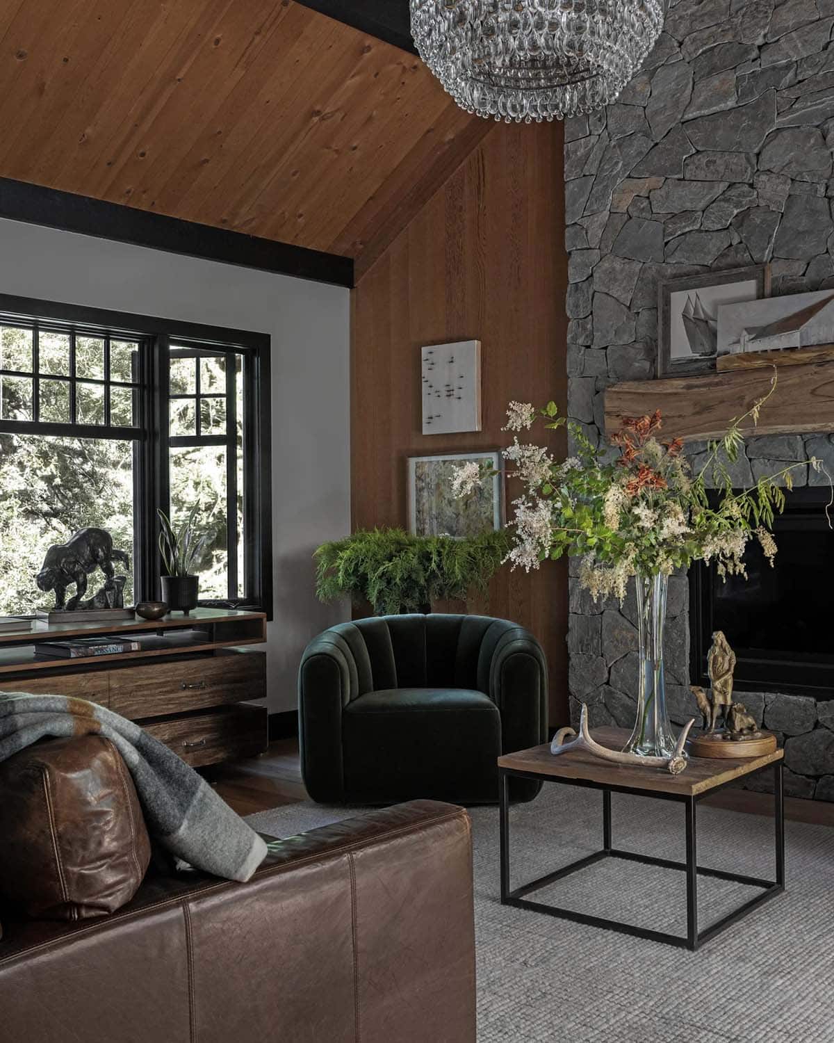 Living room corner with green velvet chair, floral arrangement, and stacked stone fireplace