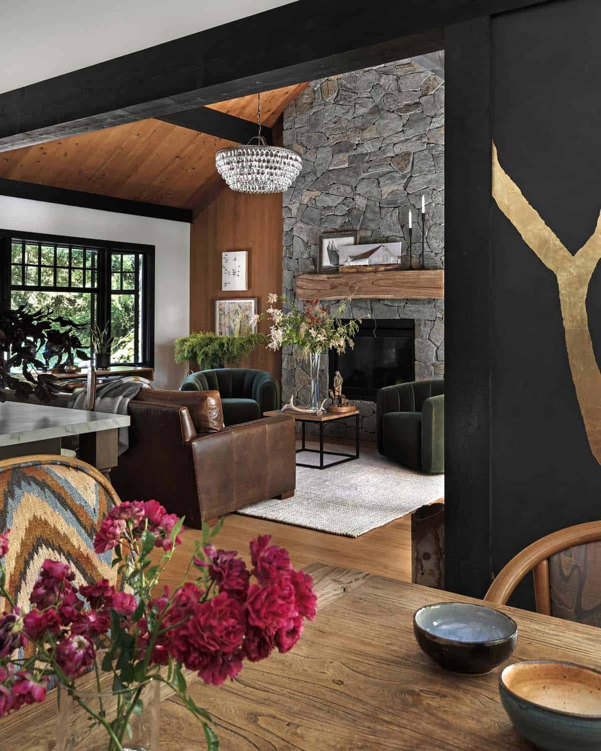 Open-plan view from dining table into wood-paneled living room with stone fireplace