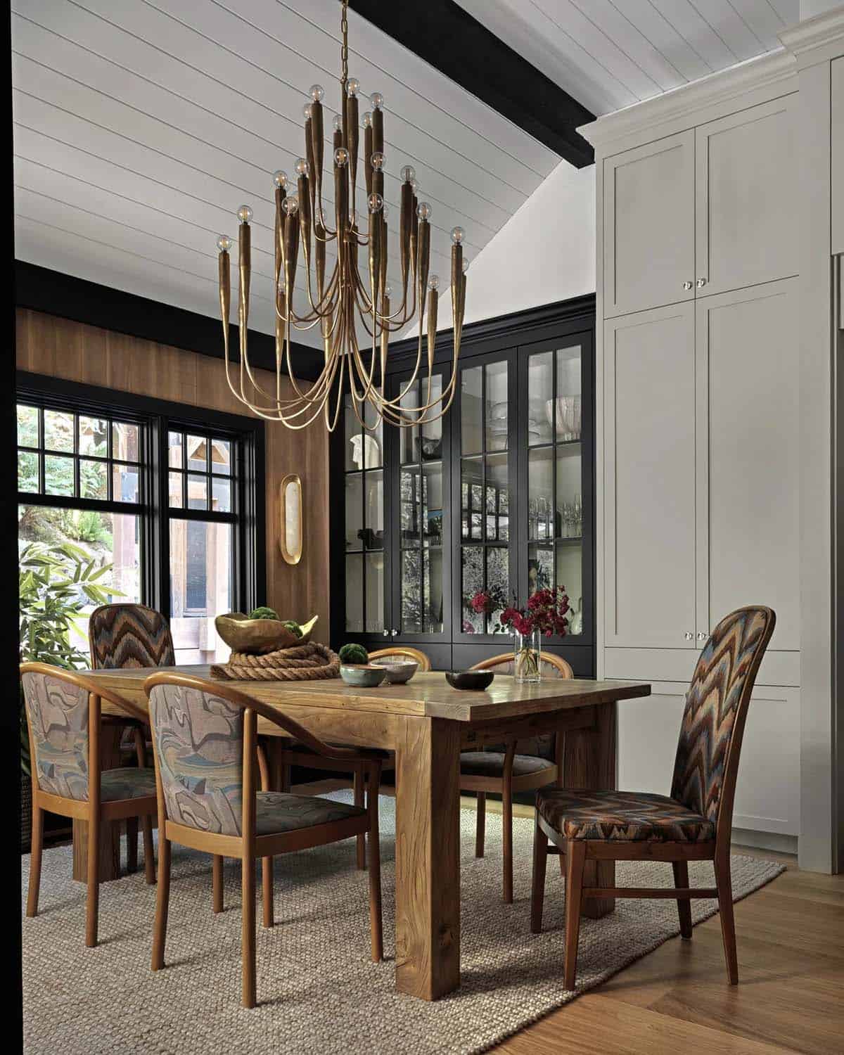 Dining area with brass candelabra chandelier, black glass-front cabinet, and patterned chairs