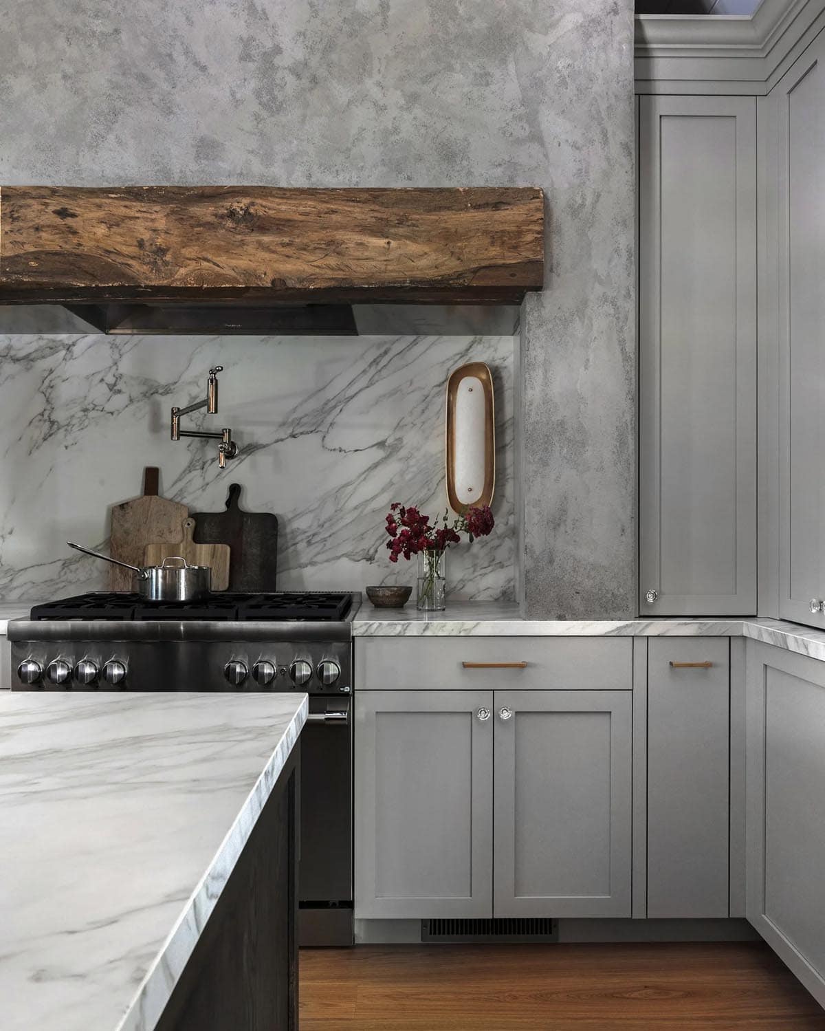 Close-up of kitchen stove, marble backsplash, gray cabinets, and brass hardware