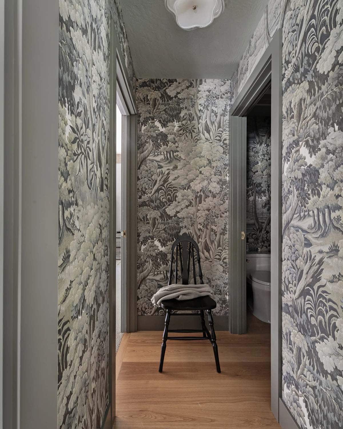 Hallway with dark botanical wallpaper, wood floor, and antique black chair
