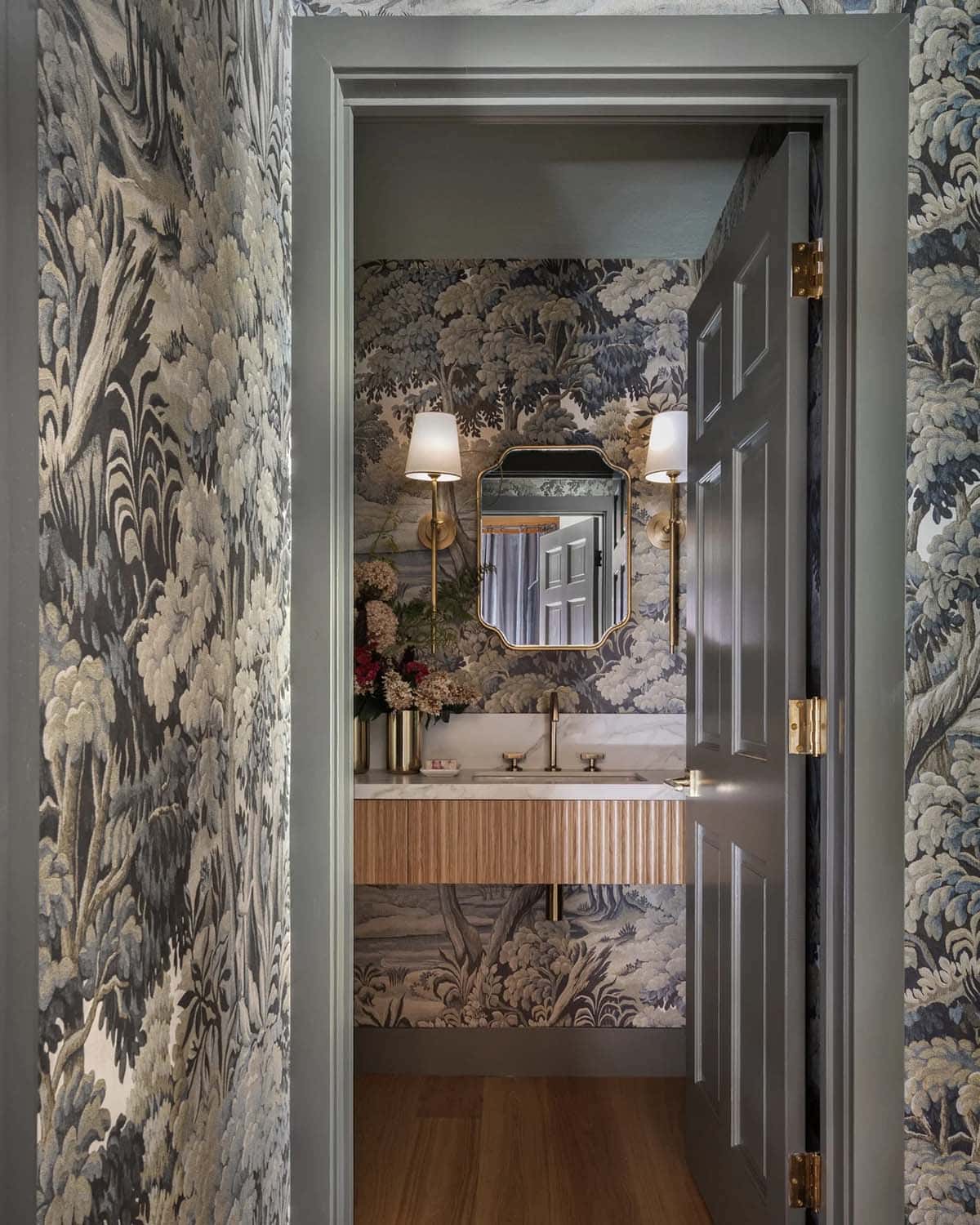 Powder room doorway with botanical wallpaper, marble vanity, and brass mirror