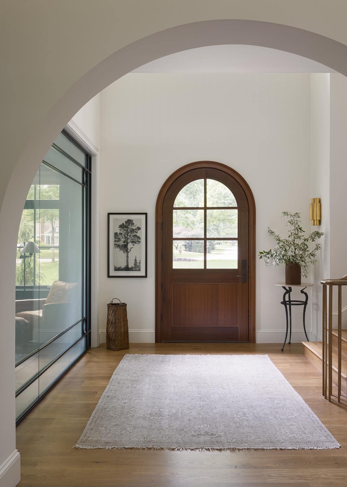 Foyer with arched wood front door, area rug, black-and-white tree print, and brass sconce