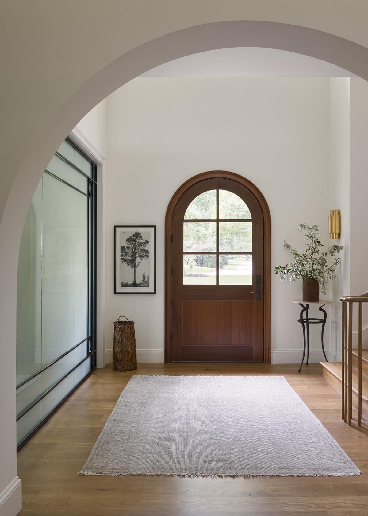 Entryway view through arched doorway toward wood front door and staircase railing