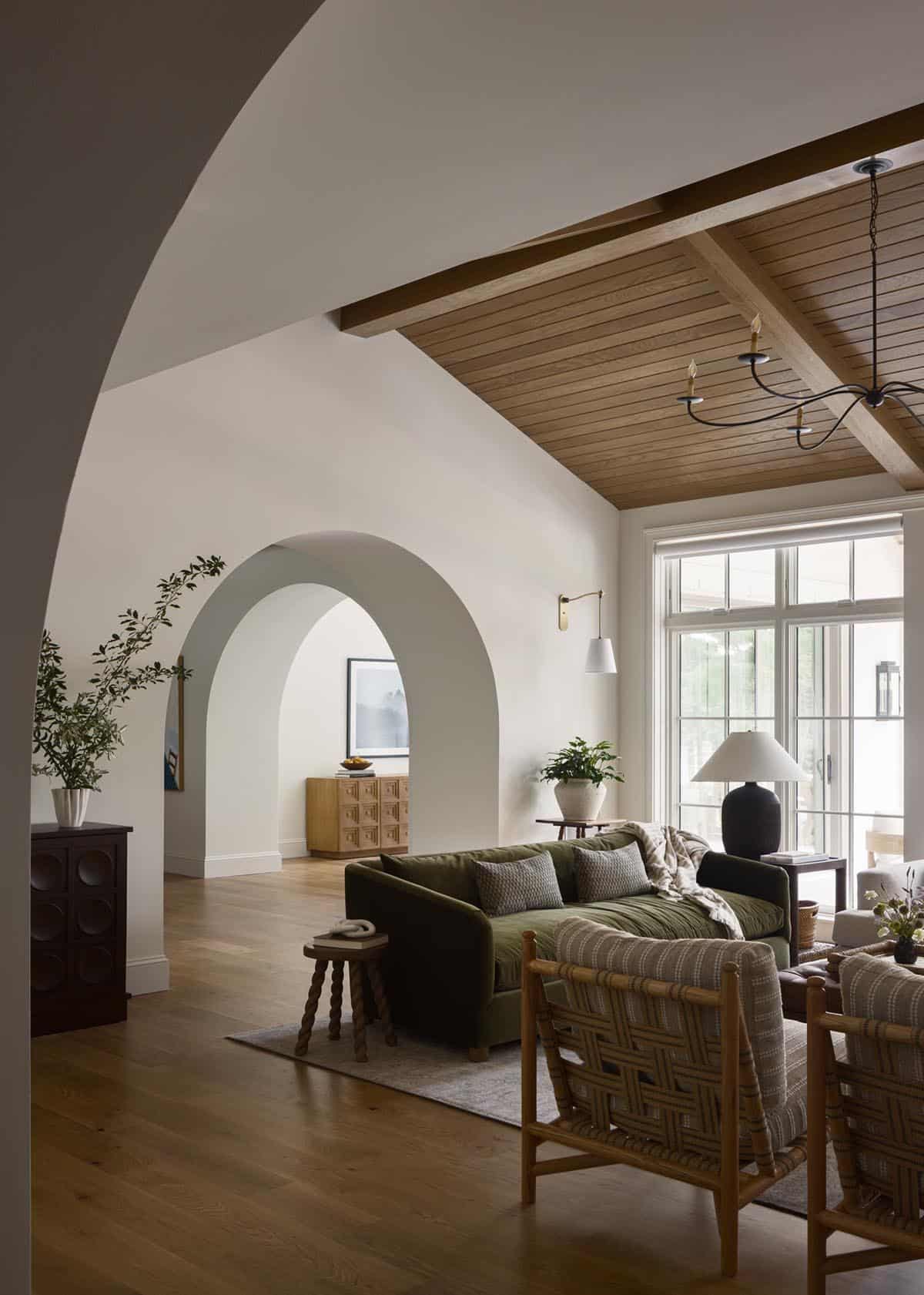 Living room with green sofa seen through curved archway, wood-beamed ceiling and glass wall