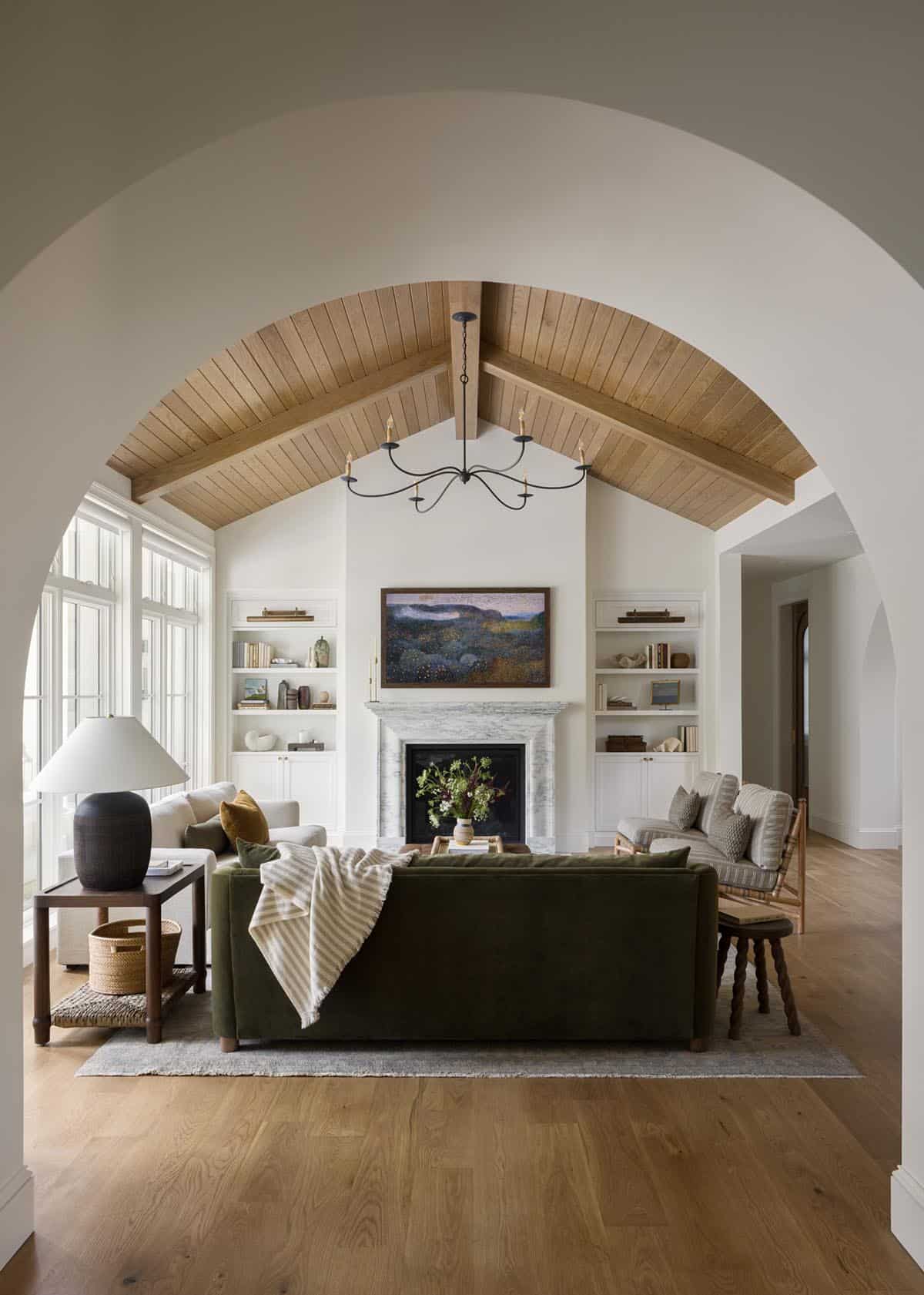 Living room with green sofa, marble fireplace, built-in bookshelves, and vaulted wood ceiling