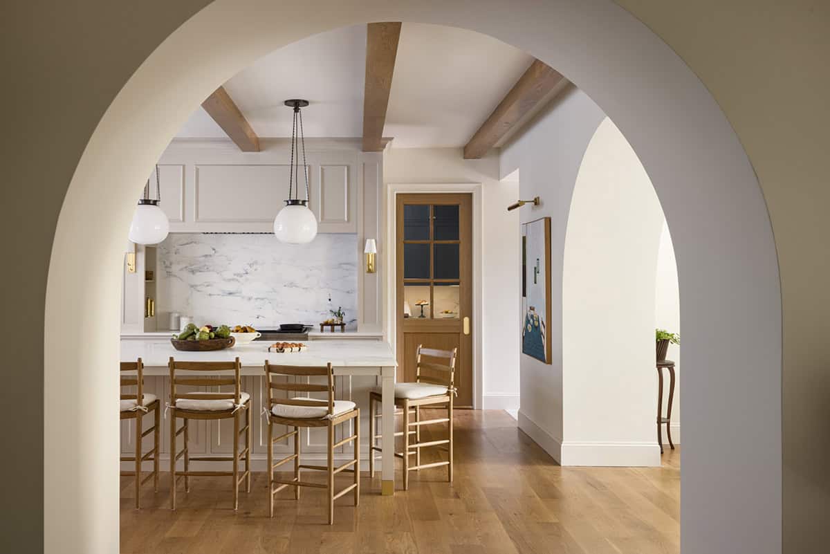 Kitchen view through arched doorways showing island, pendant lights, and marble backsplash