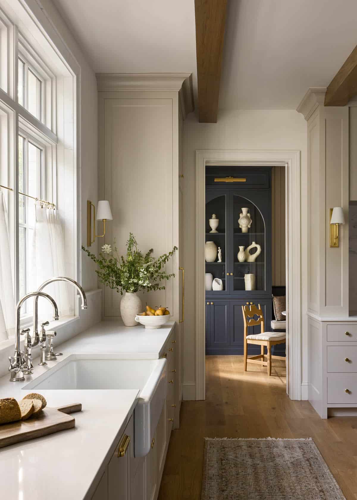 Kitchen sink area with brass faucet, flowers, and view into navy blue dining nook