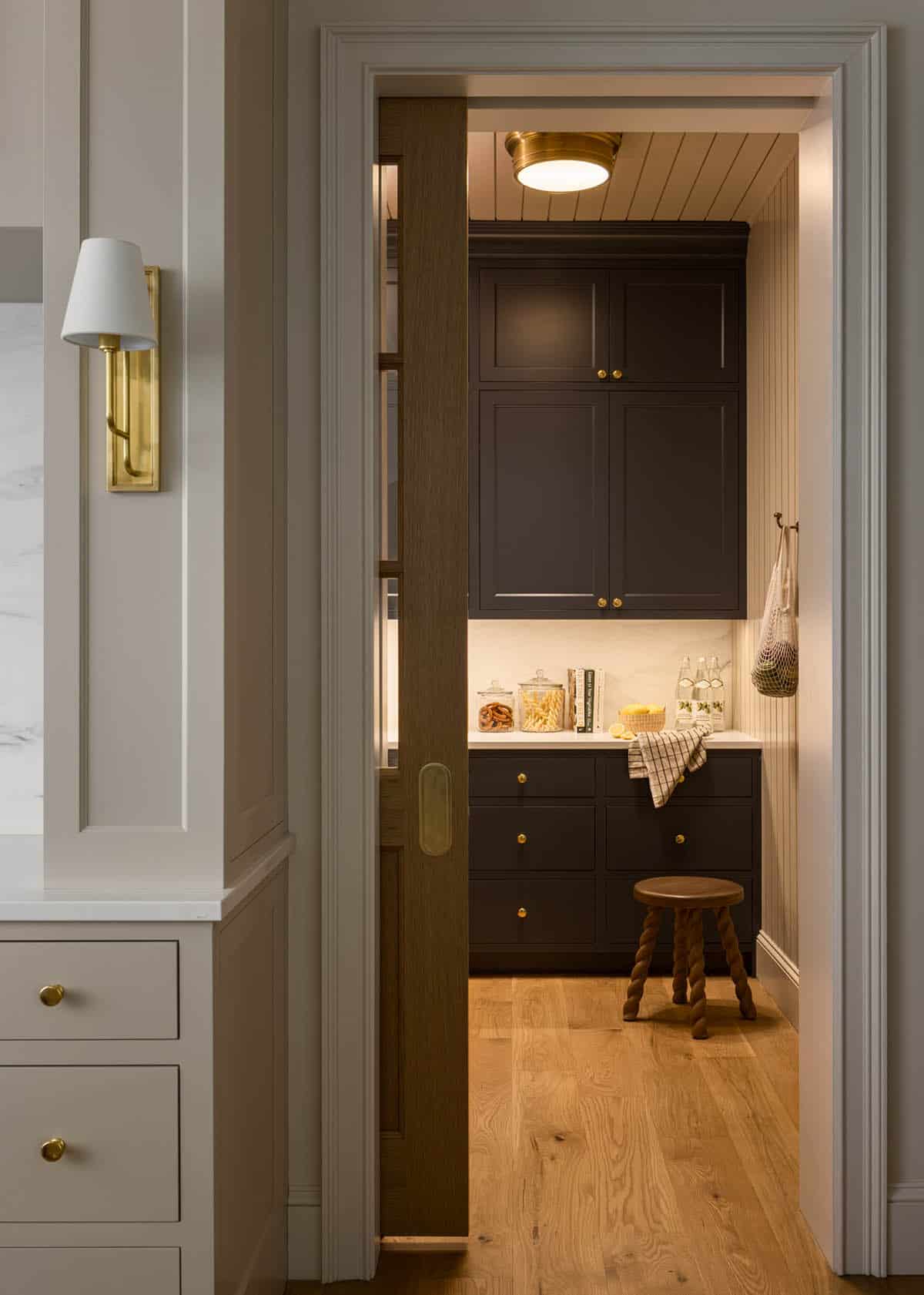 Sliding wood pocket door opening to dark pantry with marble counter and stool
