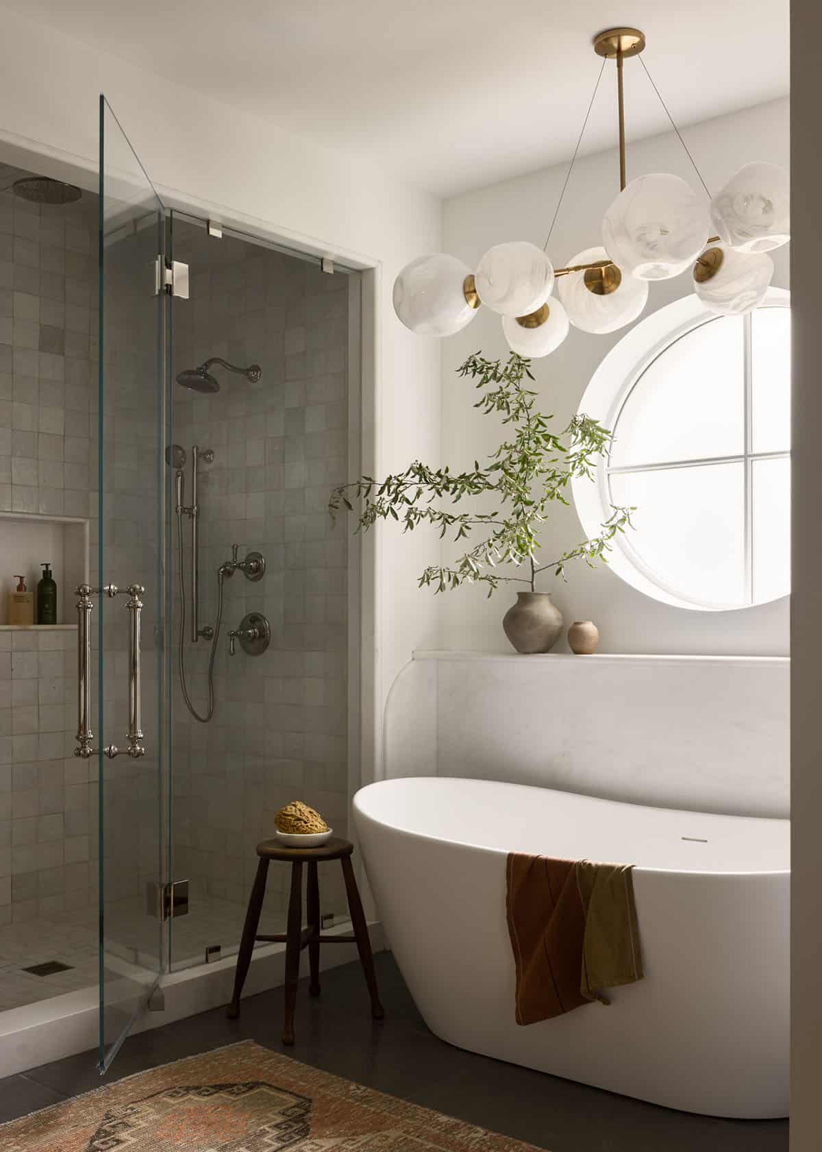 Bathroom with freestanding tub, round window, glass shower, and bubble chandelier