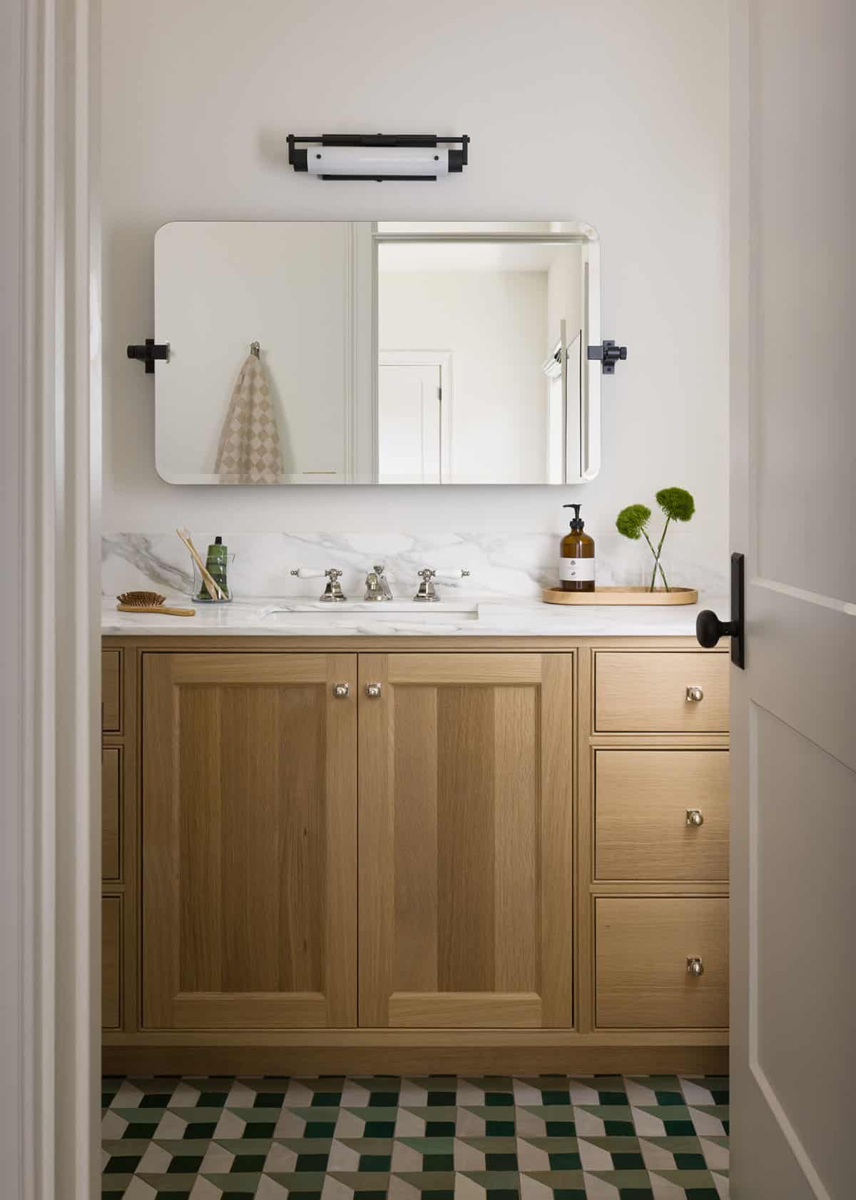 Small bathroom vanity with oak cabinets, marble counter, and geometric tile floor
