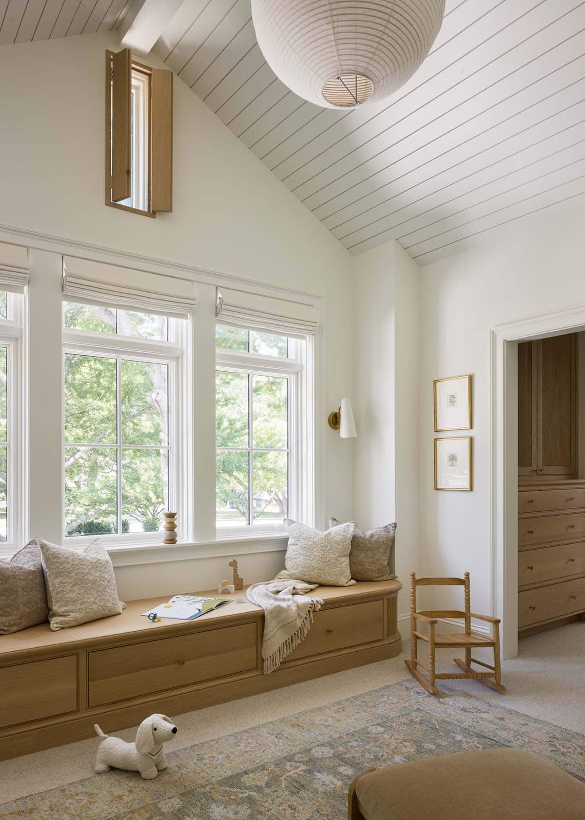 Child's bedroom window seat beneath vaulted shiplap ceiling with paper lantern light