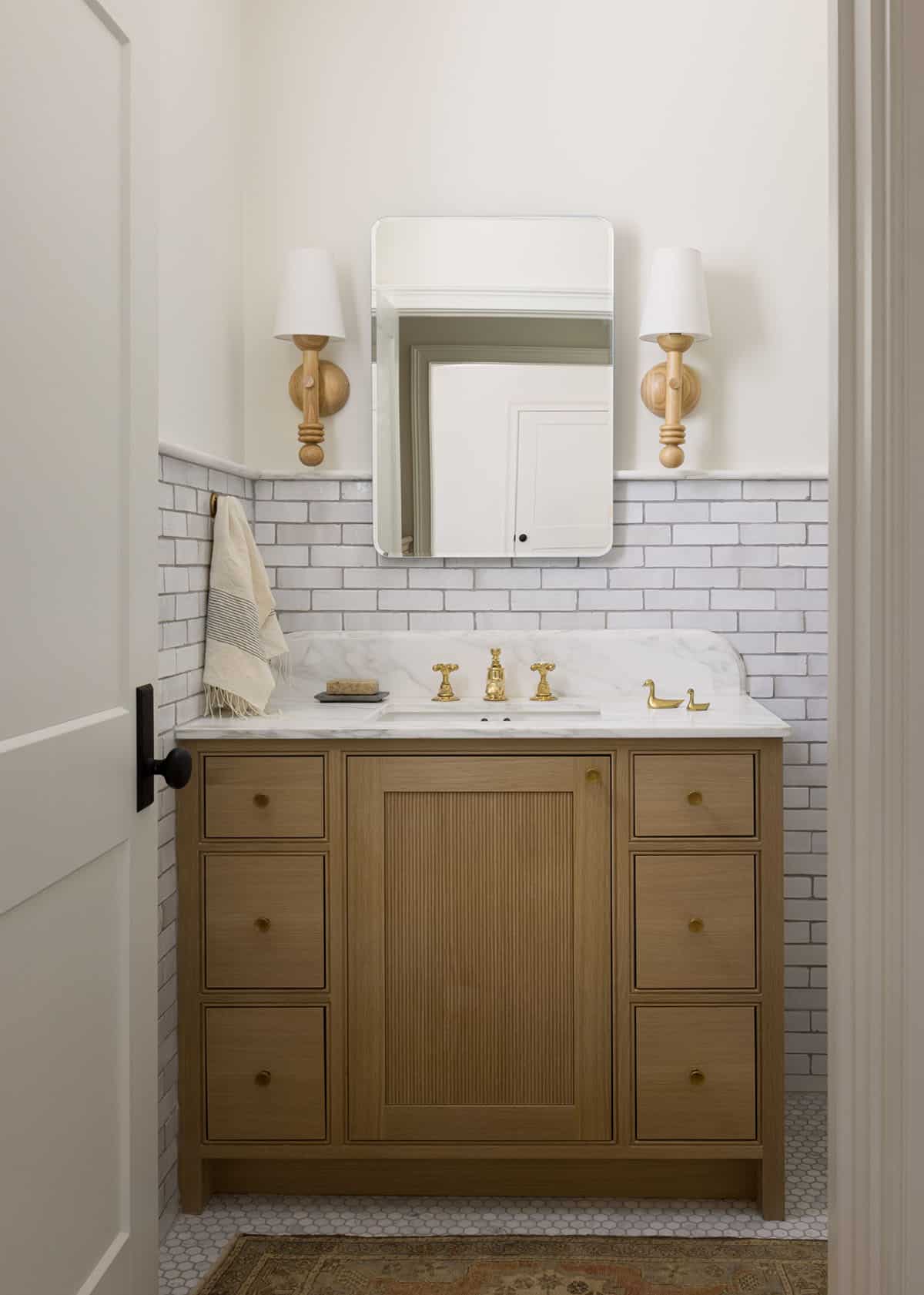 Powder room vanity with wood cabinet, subway tile, and brass duck-shaped faucet accents