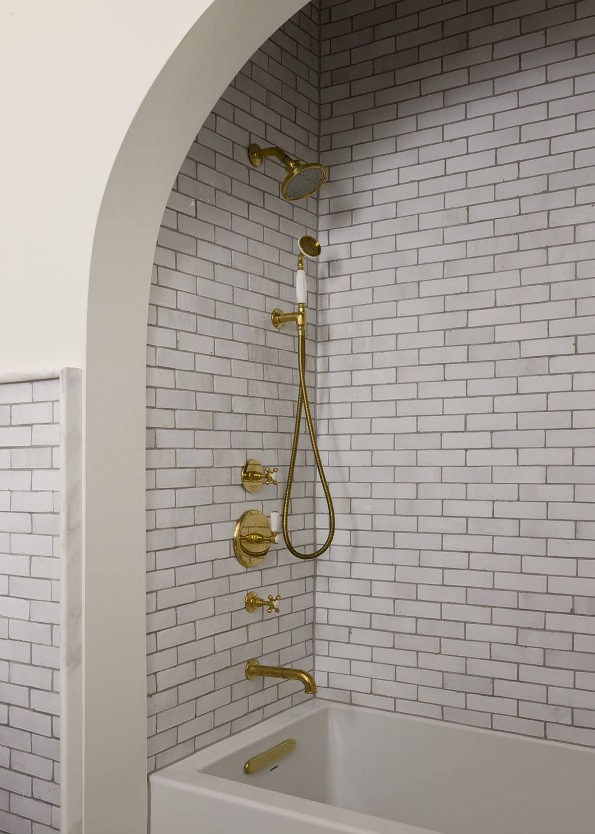 Shower fixtures with brass hardware against white subway tile backsplash