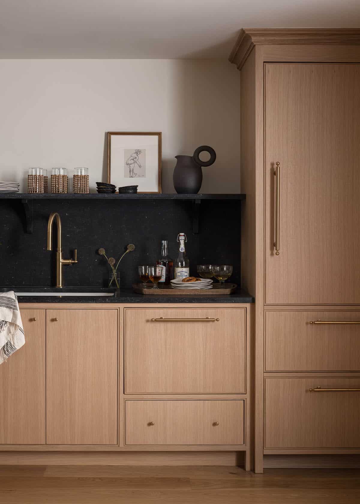Wet bar nook with black stone counter, brass faucet, and wood cabinetry