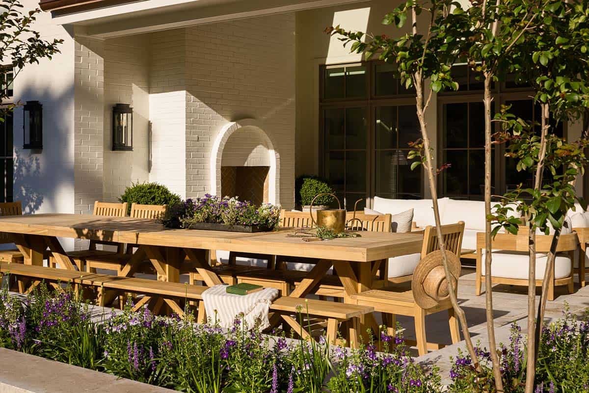 Outdoor teak dining table set with benches surrounded by purple flowering plants