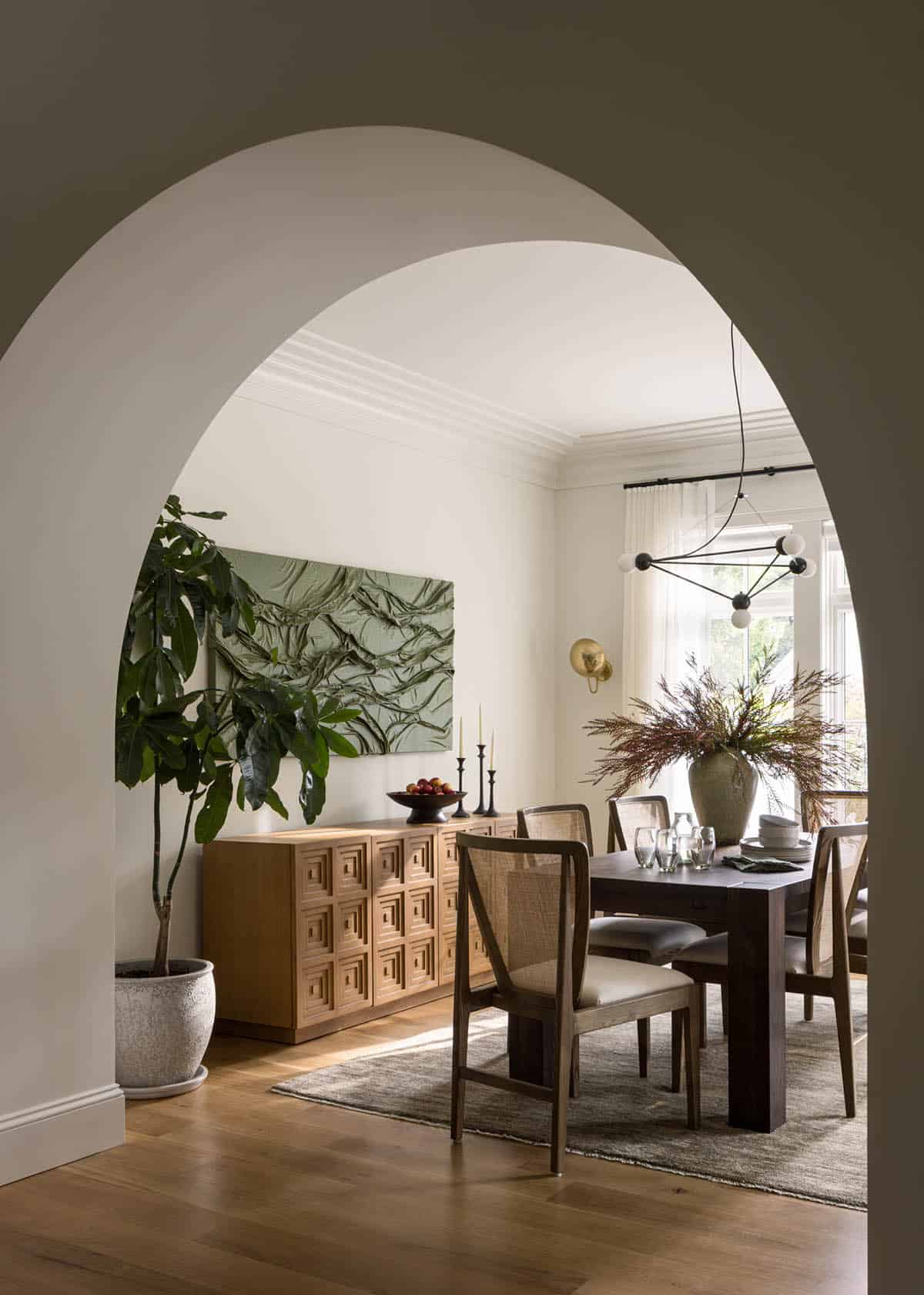 Dining room viewed through arched doorway with cane chairs and sculptural pendant light