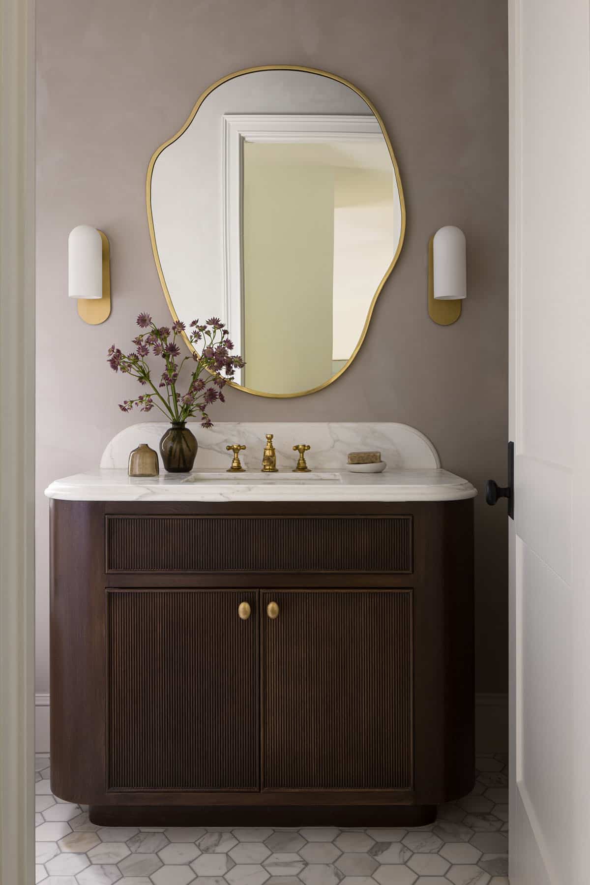 Powder room with curvy brass-framed mirror and fluted dark wood vanity