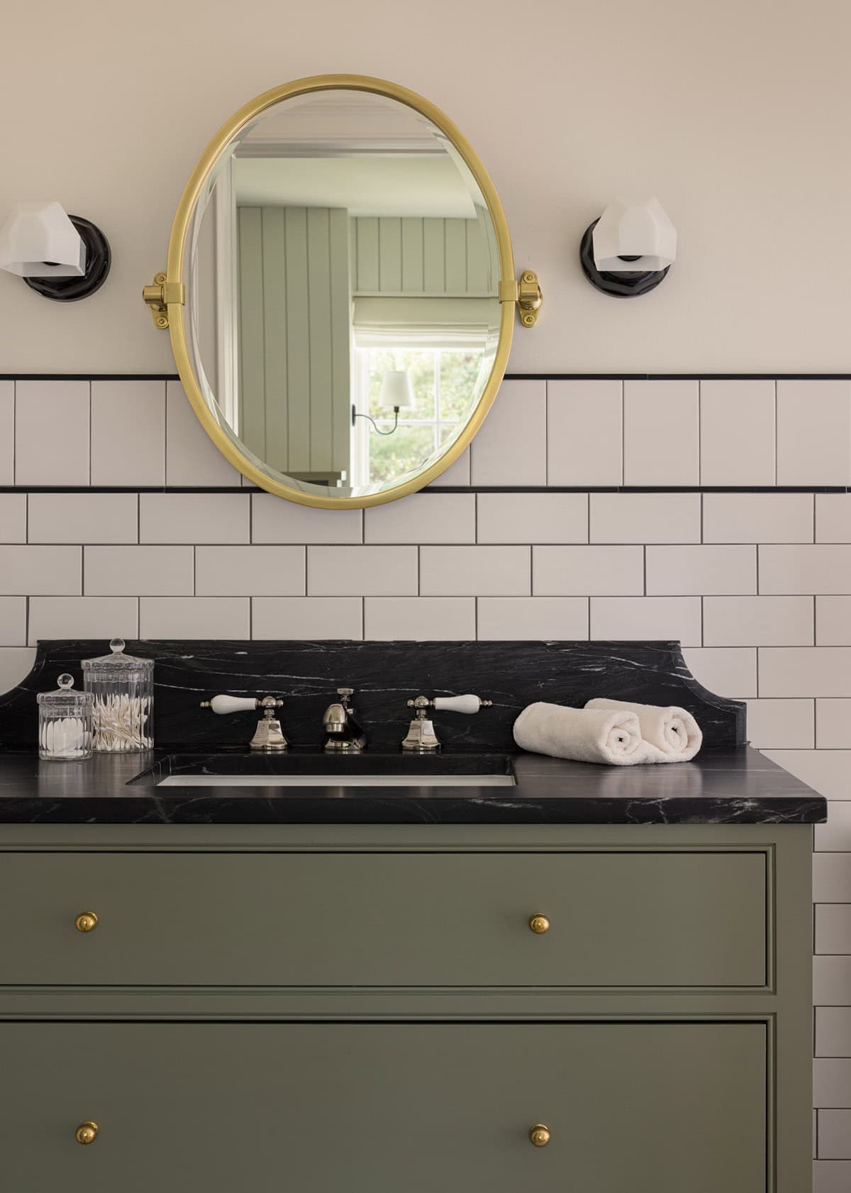 Green vanity with black marble counter, subway tile, and oval brass mirror