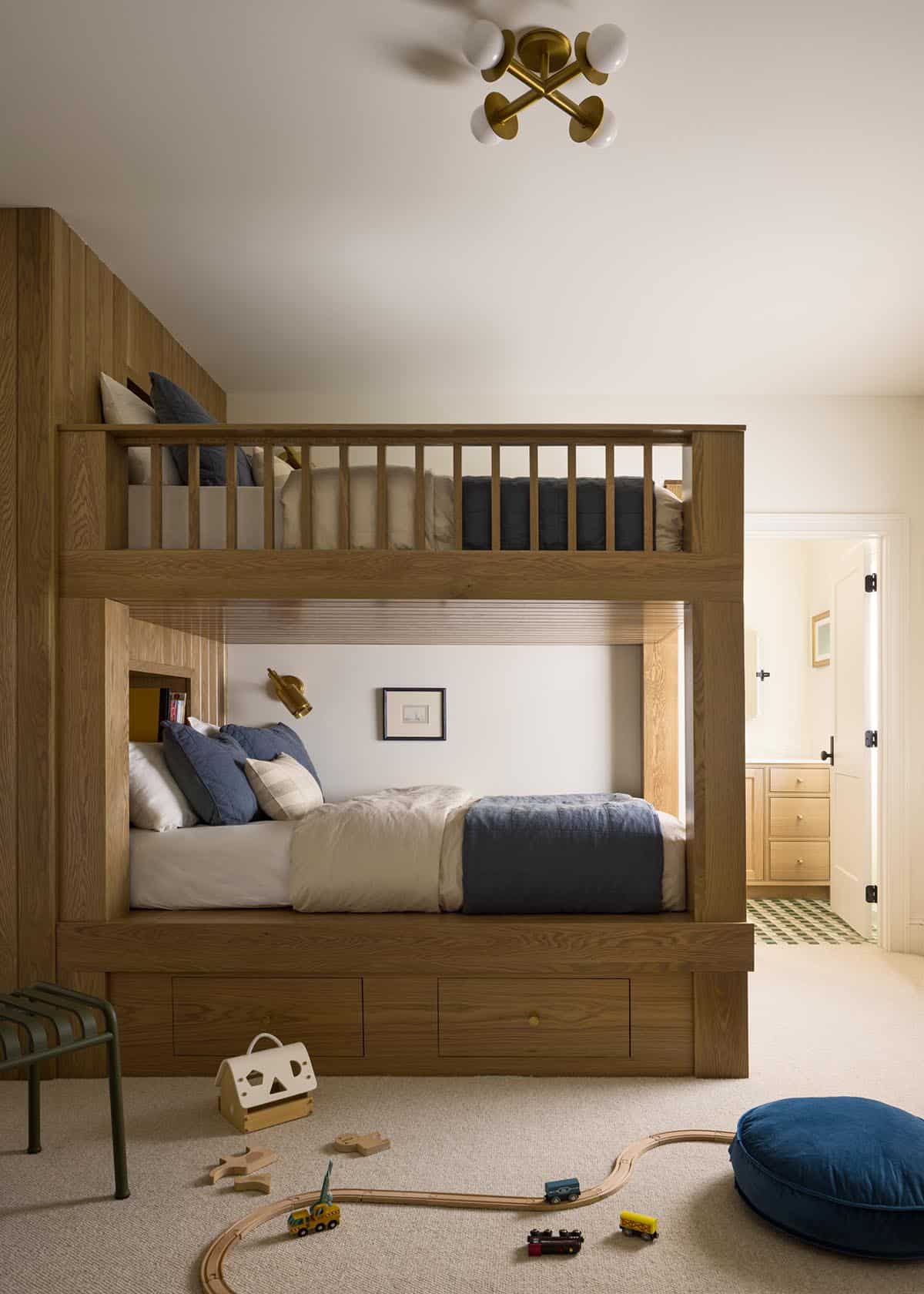 Built-in wood bunk beds in kid's bedroom with navy bedding and toy train set on floor