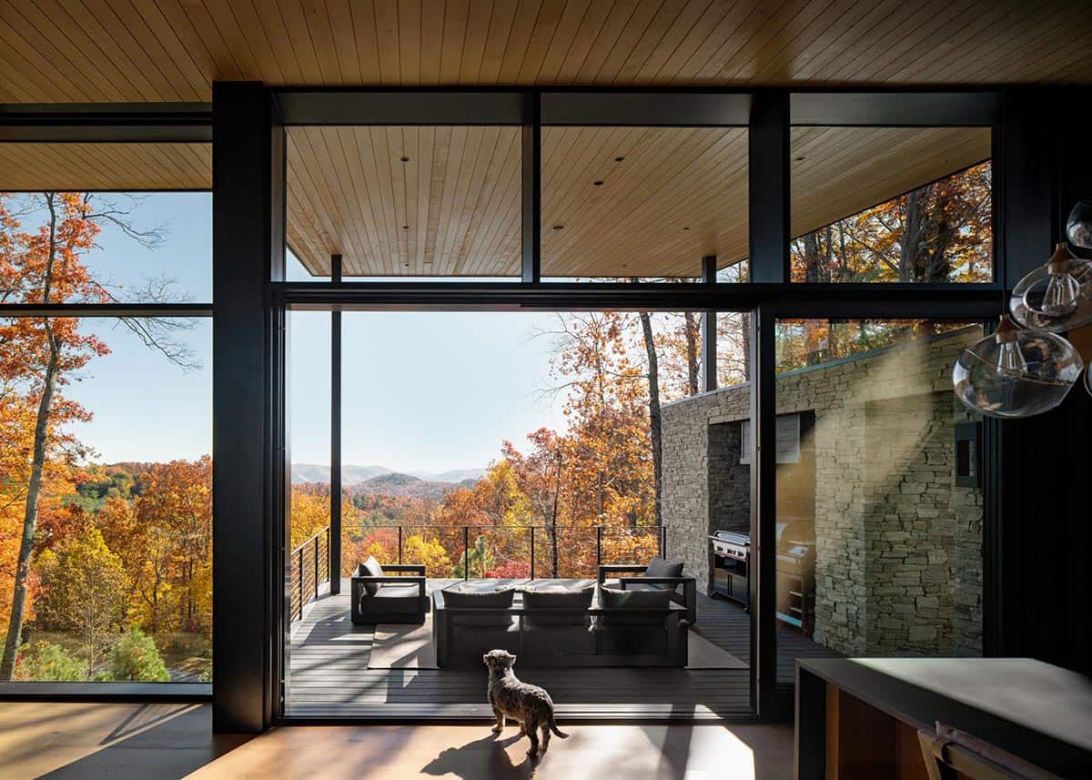 Open sliding glass doors leading to covered deck with outdoor seating and mountain views