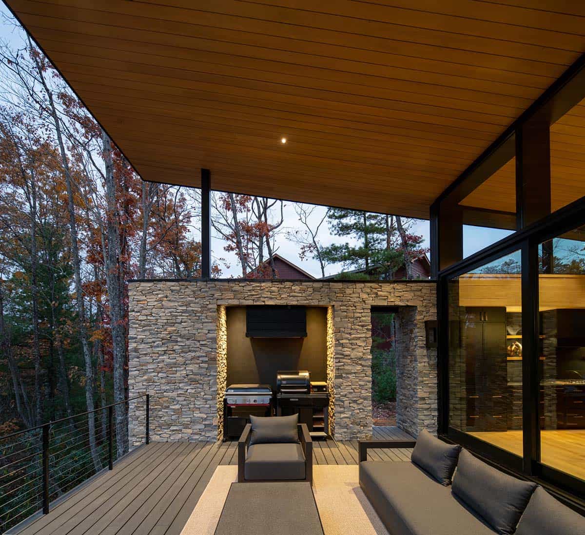 Covered outdoor kitchen and lounge deck with stone wall and built-in grill at dusk