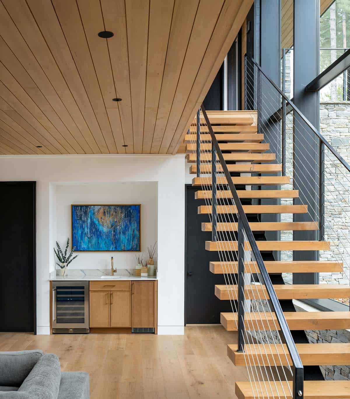 Wet bar with blue abstract art beside open-tread staircase with cable railing
