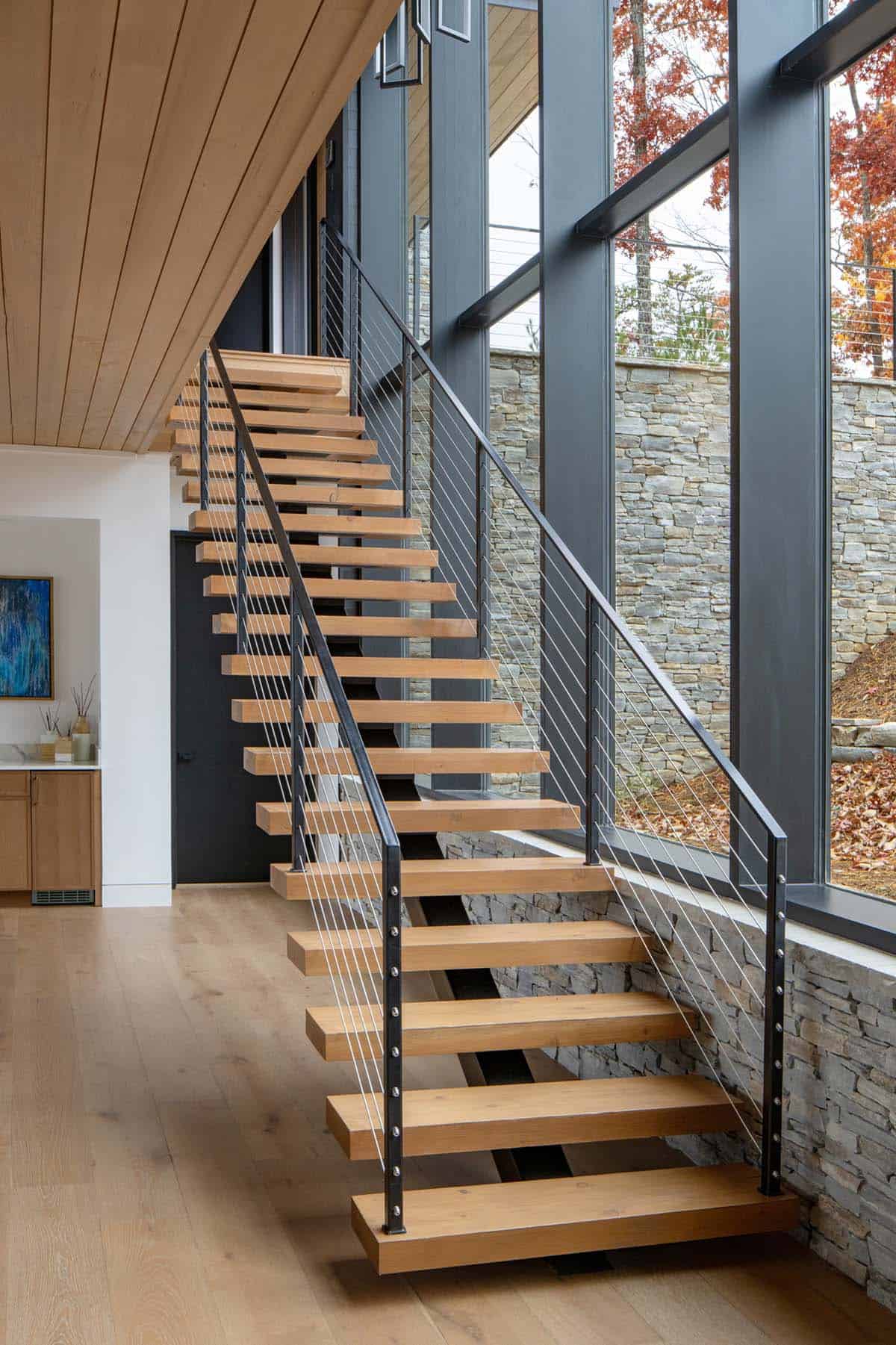 Floating wood staircase with cable railing against stone accent wall
