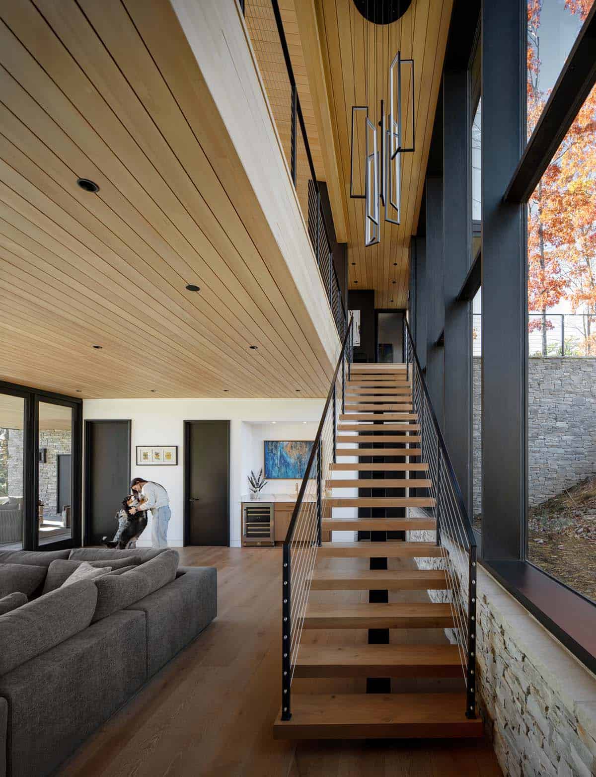 Multi-story stairwell with pendant lighting, person greeting dog on gray sofa