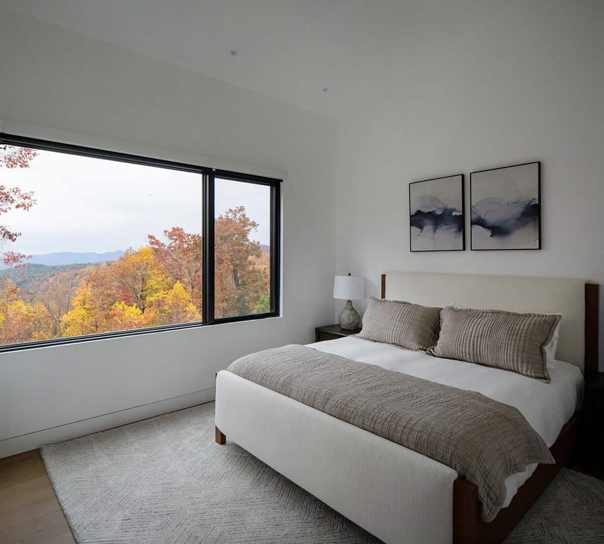 Bedroom with upholstered bed and large window overlooking mountain fall foliage