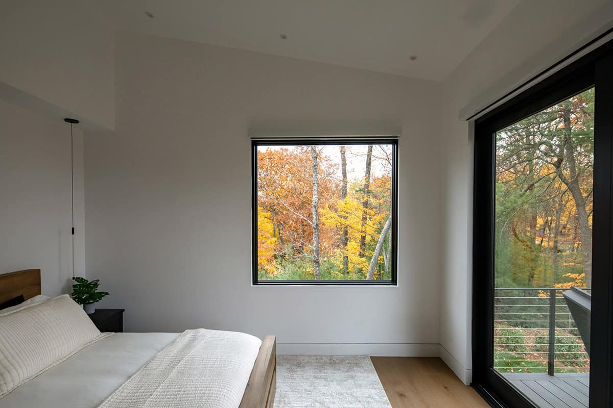 Bedroom corner with sliding glass door to balcony amid autumn trees