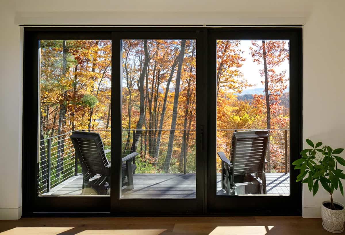 Sliding glass doors framing deck loungers and colorful fall forest view