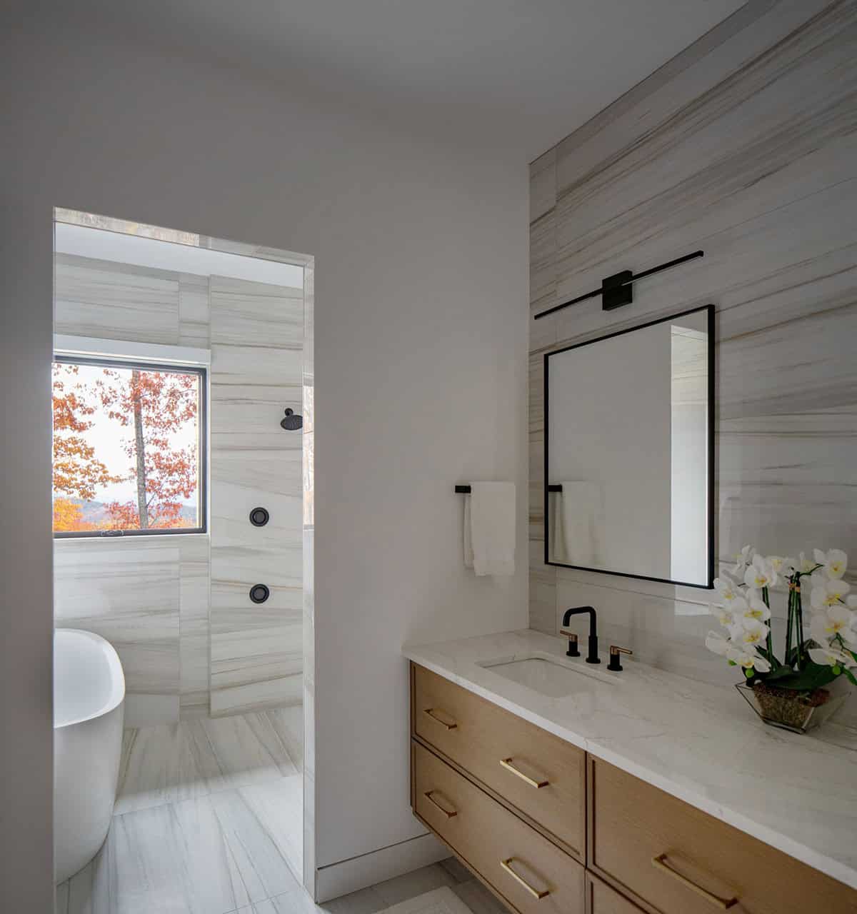 Bathroom with marble tile, floating vanity, and view through doorway to freestanding tub