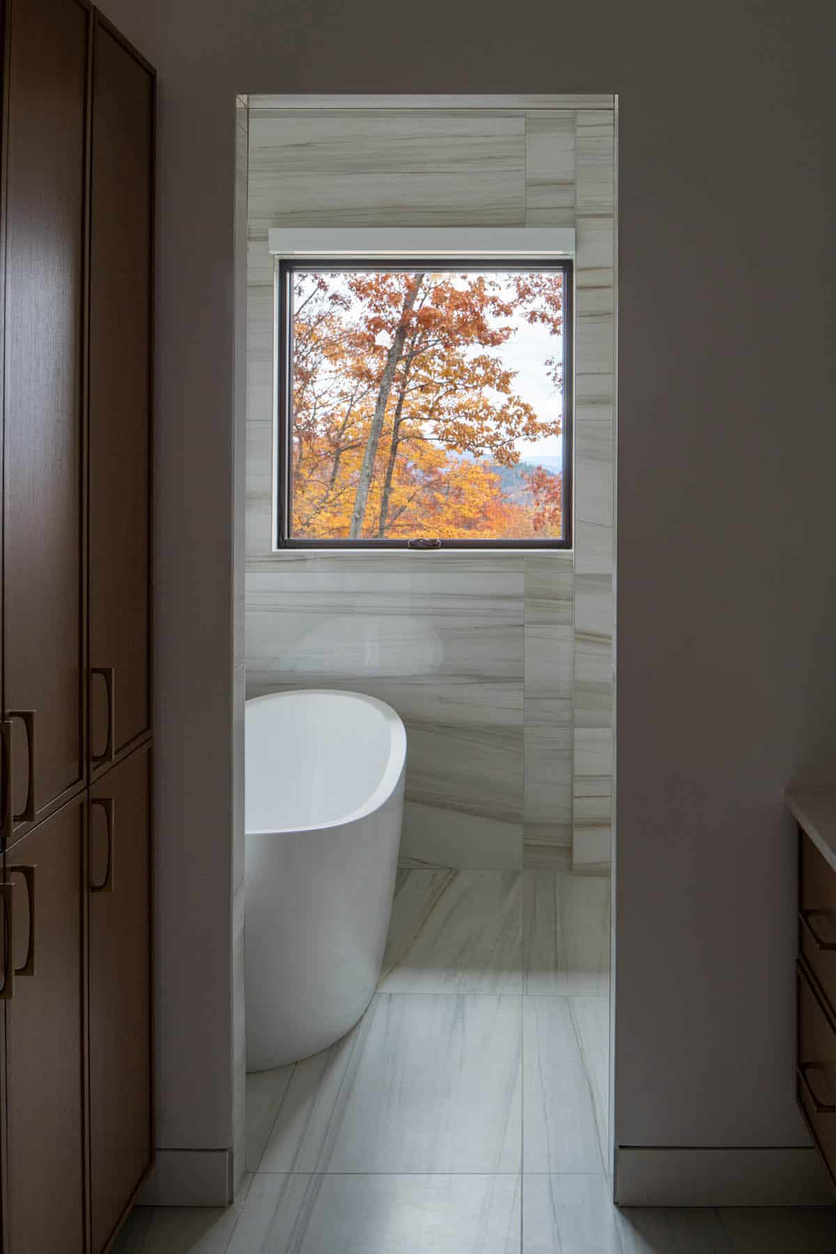 Doorway framing freestanding soaking tub beneath window with fall foliage view