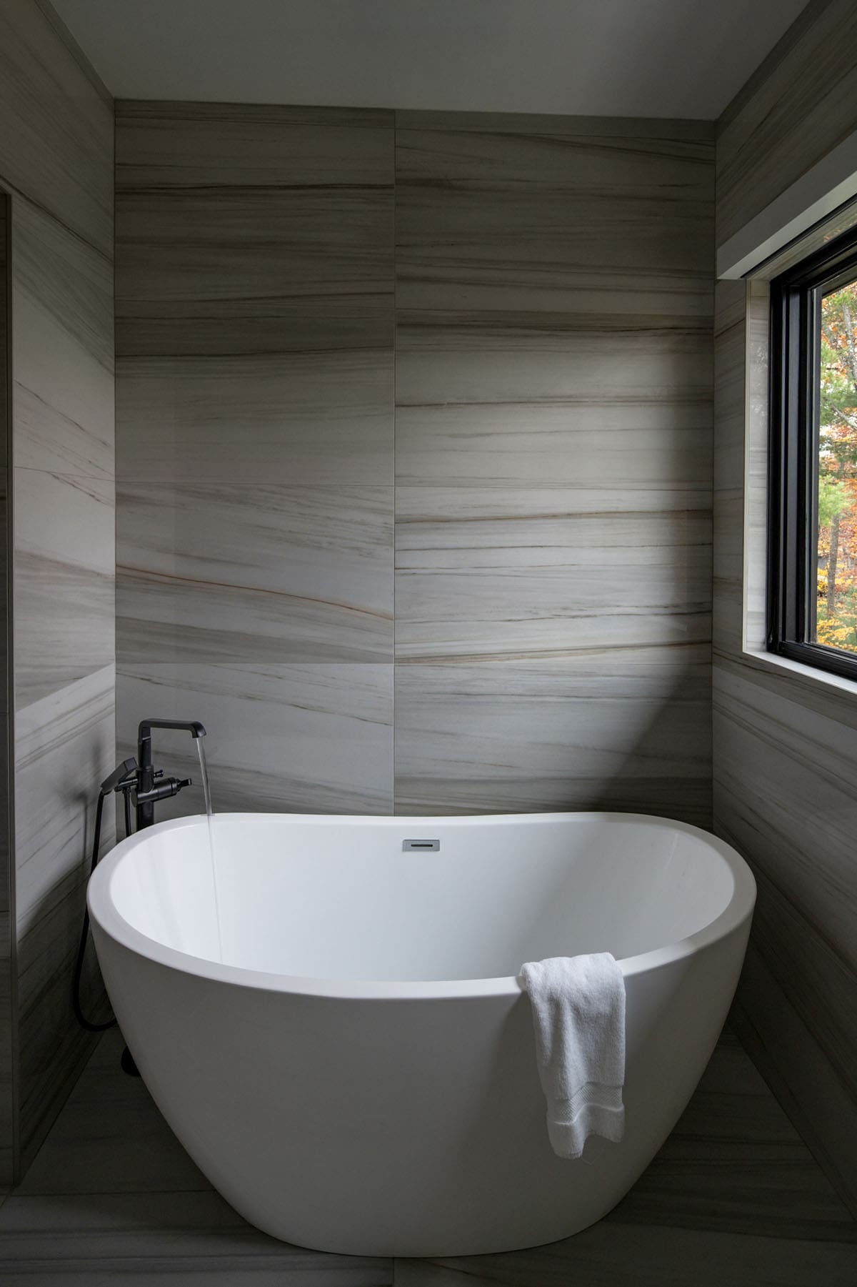 Freestanding oval tub with black floor-mount faucet against marble tile wall