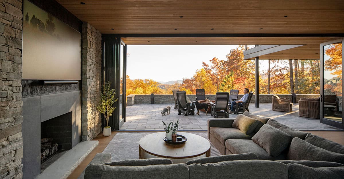 Living room opening onto stone patio with fire pit and mountain view at golden hour