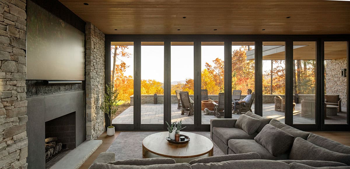 Sectional sofa facing fireplace and folding glass doors open to terrace at sunset
