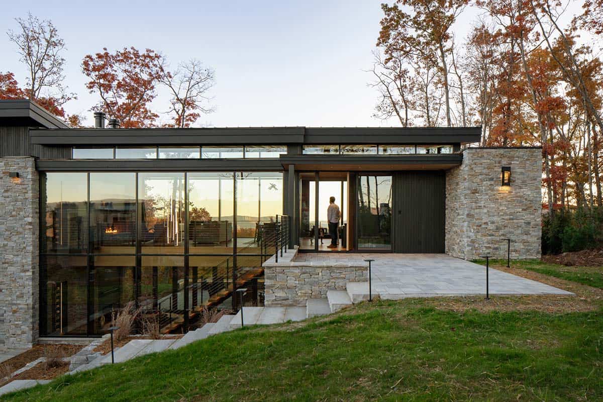 Rear exterior of modern home with stone base, black cladding, and glass walls at dusk