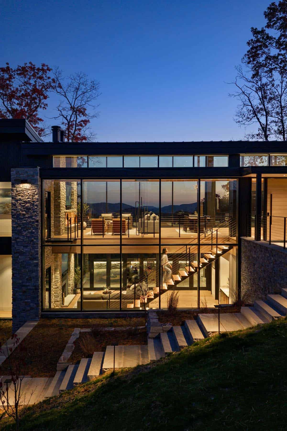 Illuminated glass facade showing staircase and living spaces at twilight