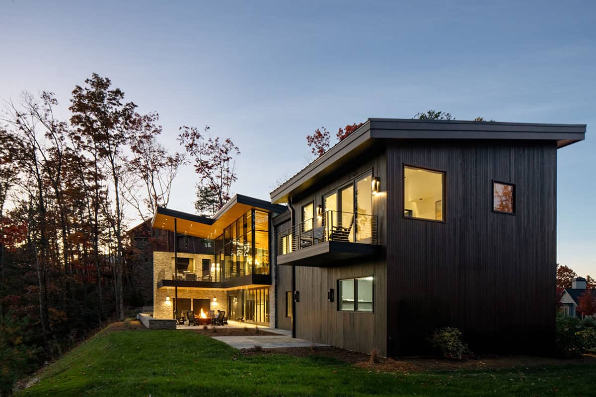 Rear elevation of multi-level mountain home with lit patio and fire feature at dusk