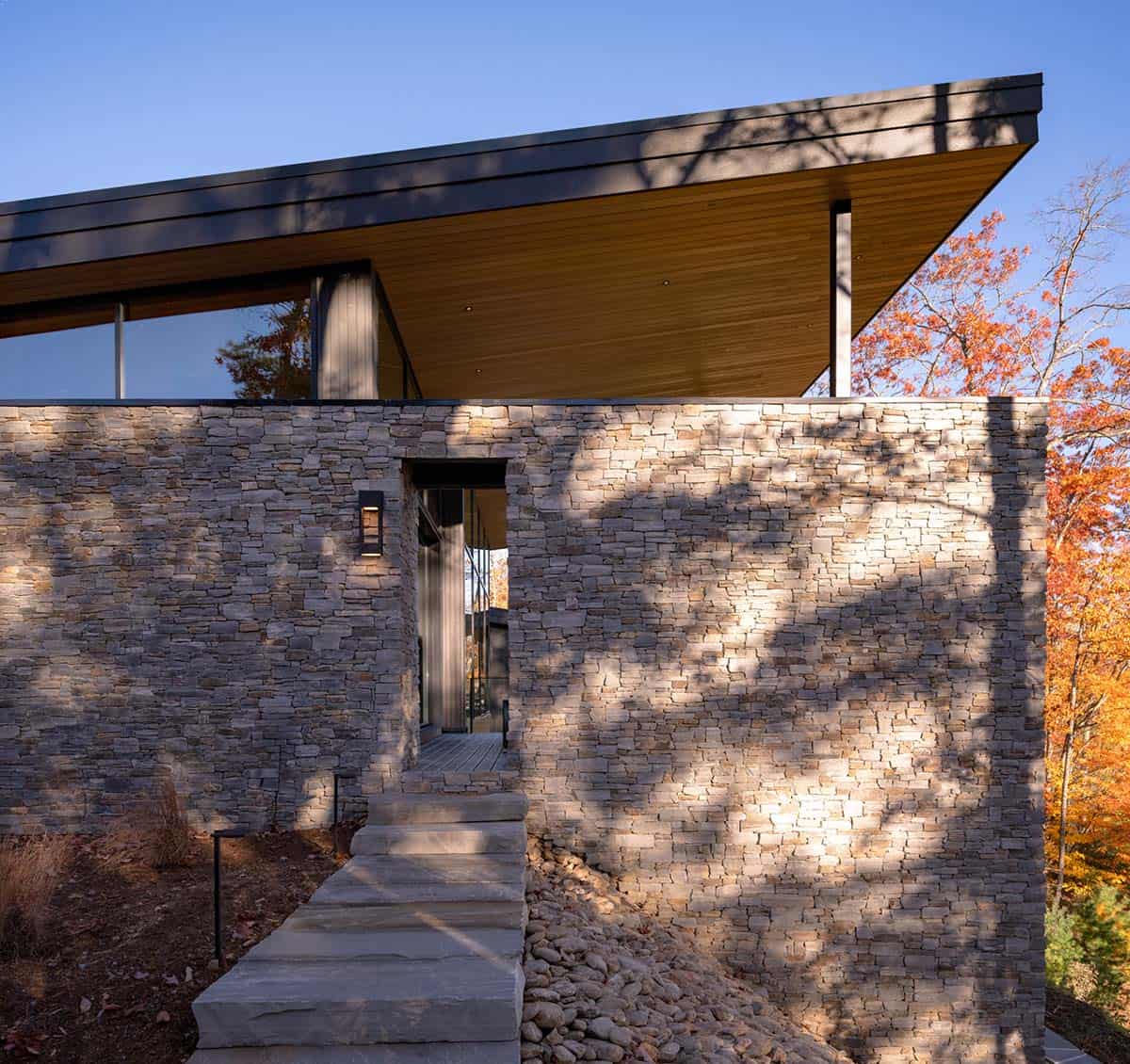 Stone entry walkway leading to home beneath cantilevered wood roof overhang