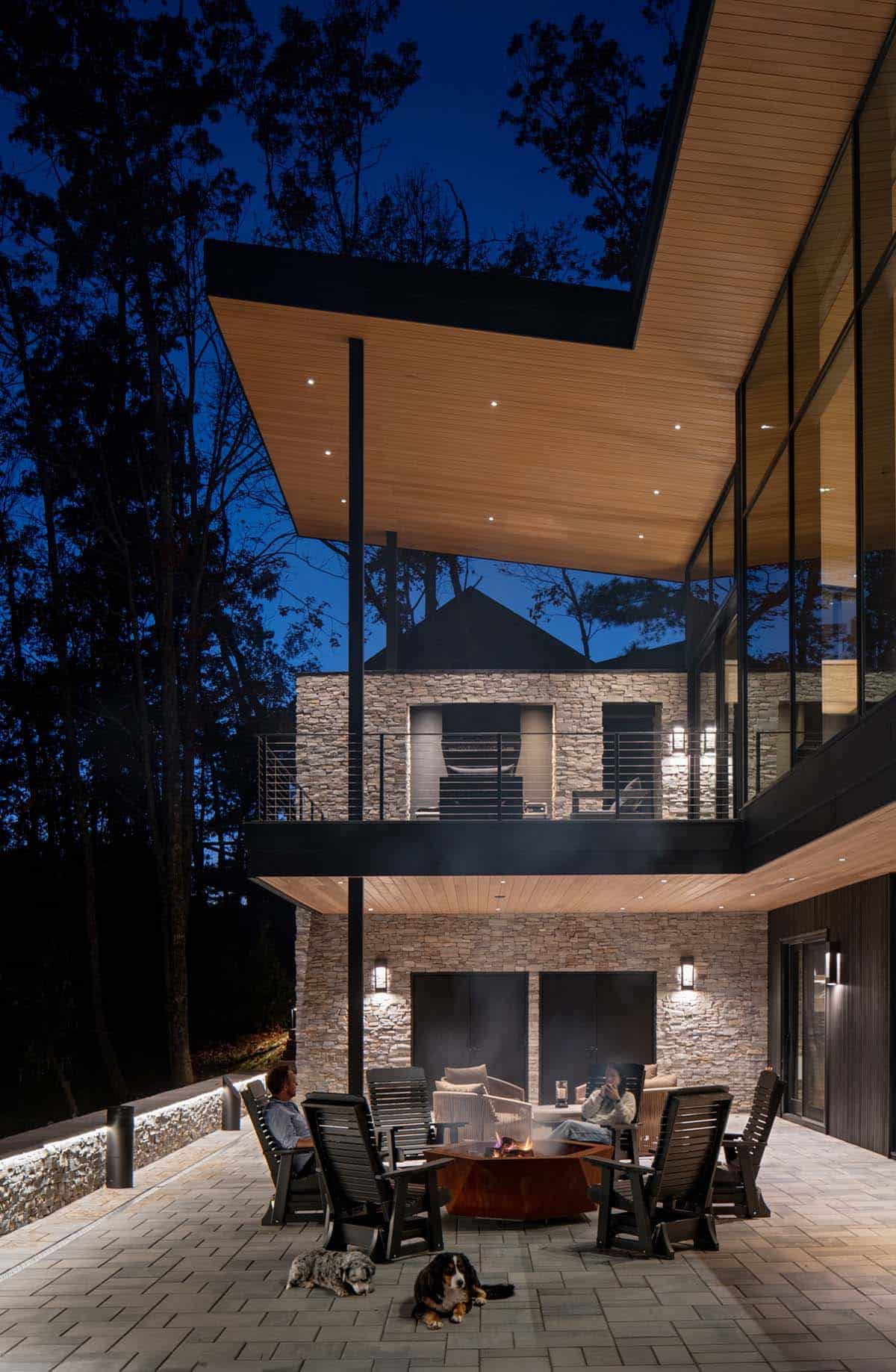 Multi-level stone and glass home exterior with fire pit patio at night